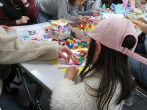福岡女子短期大学の子ども学科のブースで、子供が折り紙体験をし、机の上に色とりどりの折り紙作品が置かれている様子