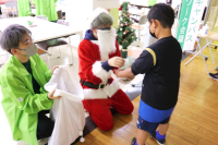 サンタさんに扮した男子学生が子供にお菓子とビンゴカードが入った袋を渡しているところ