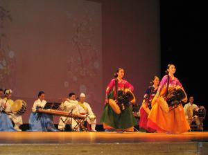 文化交流公演の写真。プラムカルコア太宰府のステージで、韓国から来た忠南国楽団が民族衣装着て伝統音楽を奏でる様子。